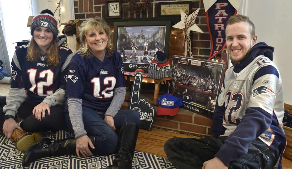 Members of the Mark and Deb Tanner family, hardcore fans of the New England Patriots, gather around a team memorabilia display at their home in Skowhegan on Monday. Deb Tanner, center, is flanked by children Kaley and Josh. Her husband, the Rev. Mark Tanner, is out of state this week, but picked the correct score of the AFC championship game against the Kansas City Chiefs.