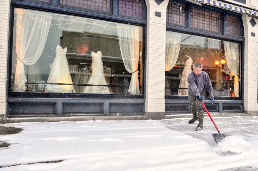Danny Fossett pushes snow off the sidewalk around 7:30 a.m. Wednesday in front of The Dreams Bridal Boutique and Tuxedo Center on Water Street in downtown Augusta.