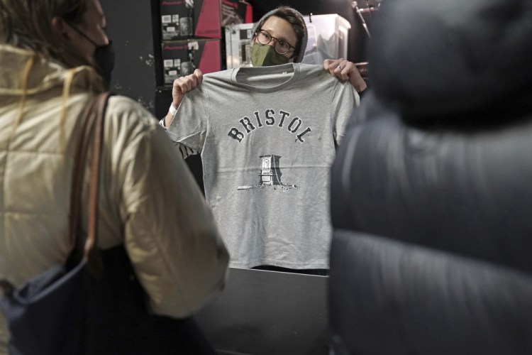 A person inside Rough Trade in Bristol, England, Saturday Dec. 11, 2021, holds up a T-shirt designed by street artist Banksy, being sold to support four people facing trial accused of criminal damage in relation to the toppling of a statue of slave trader Edward Colston. (Jacob King/PA via AP)