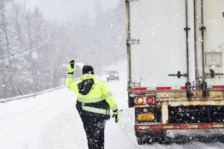 Brattleboro, Vt., police Officer Ryan Washburn helps direct traffic on Route 9 after a tractor-trailer got stuck in the snow during a snowstorm on Monday.