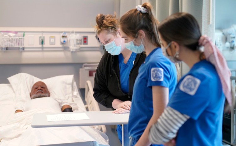Nursing students Anna Britton, Lea Yenawine and Marlaina Stickney, left to right, look over paperwork before starting a training exercise in a simulation hospital room with a lifelike mannequin patient, seen at left, at the University of Southern Maine.