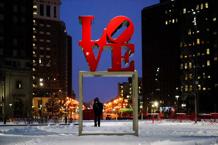 A person wearing a face mask as a precaution against the coronavirus walks during a winter storm near the Robert Indiana sculpture "LOVE" at John F. Kennedy Plaza, commonly known as Love Park, in Philadelphia, Monday, Feb. 1, 2021. 