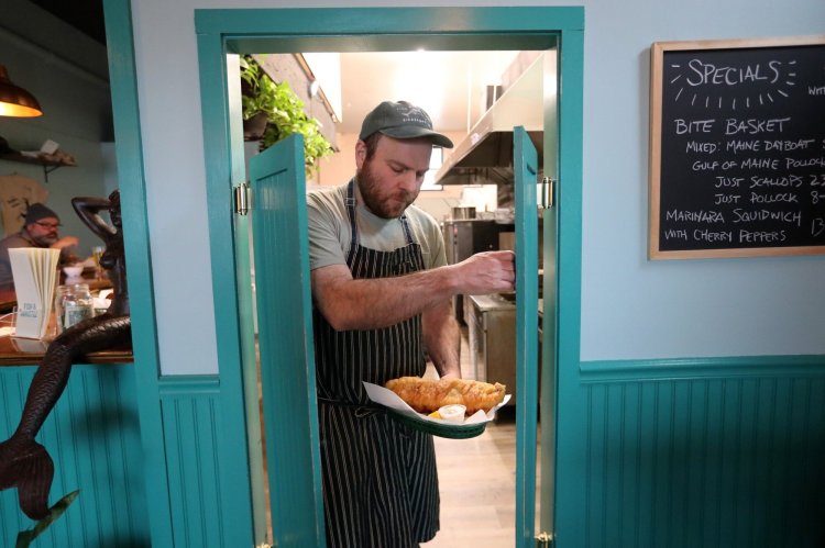 Jason Eckerson, chef and co-owner at Fish & Whistle, emerges from the kitchen with a large basket of fish and chips. The dish, along with smash burgers and fried chicken sandwiches, are having a moment on menus around the region. 